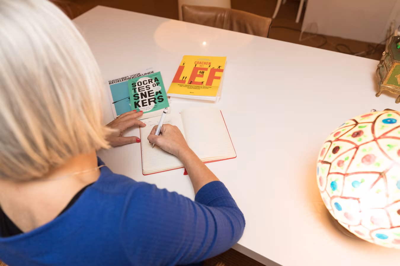Bovenaanzicht van een persoon die schrijft in een leeg notitieboekje aan een witte tafel met boeken socrates of snekers en doodles of l.e.f, werkwijze leren en ontwikkelen